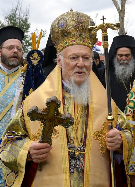 Ecumenical Patriarch Bartholomew I in gold vestments and jewelled mitre, holding a blessing cross and crozier, flanked by Orthodox clergy